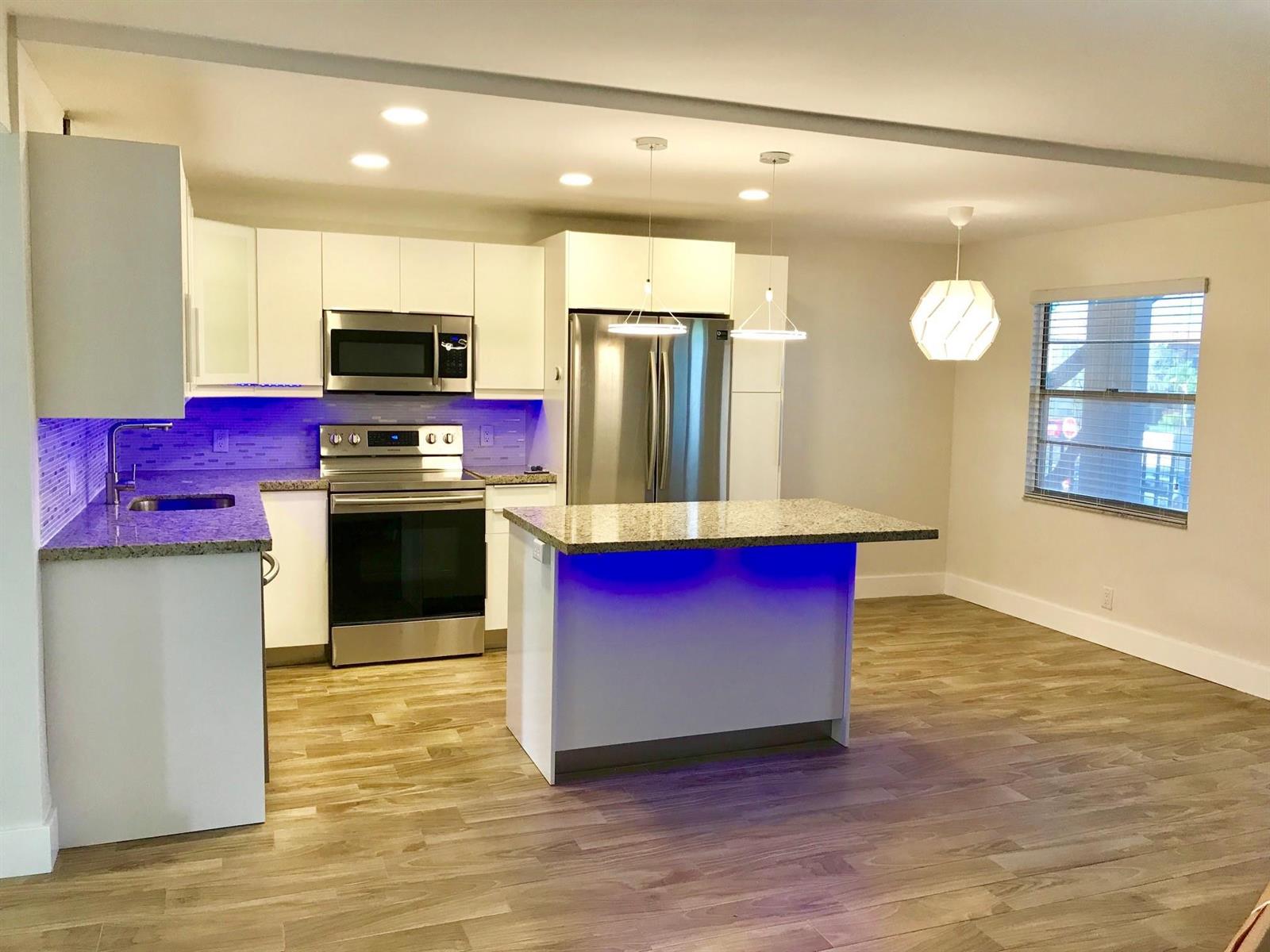 A modern kitchen features white cabinets, granite countertops, stainless steel appliances, and blue accent lighting — 300 SW 134th Way # E210, Hollywood FL 33027, HOLLYWOOD, FL