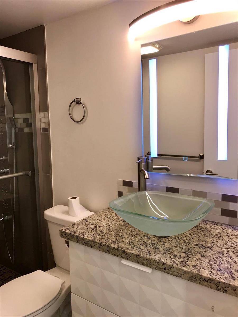 A bathroom with a granite countertop, vessel sink, illuminated mirror, and a glass shower enclosure — 300 SW 134th Way # E210, Hollywood FL 33027, HOLLYWOOD, FL