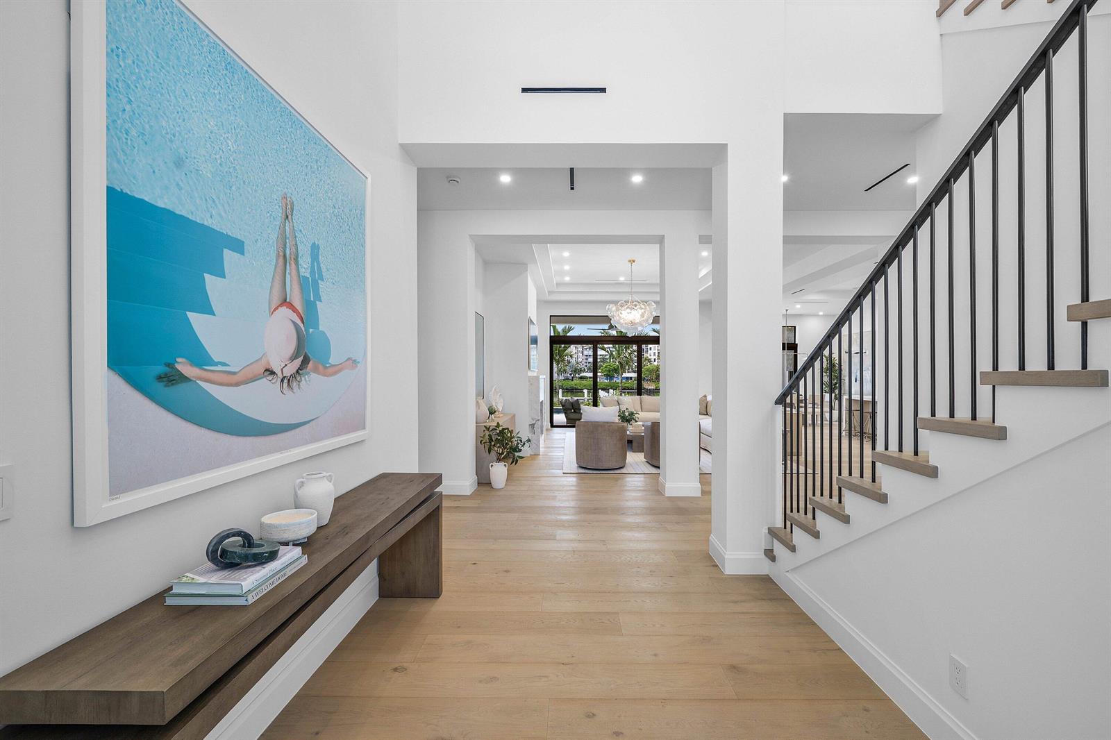A bright entryway features light wood floors, a modern staircase, and a large pool-themed artwork — 908 N Atlantic Drive, Lantana FL 33462, LANTANA, FL