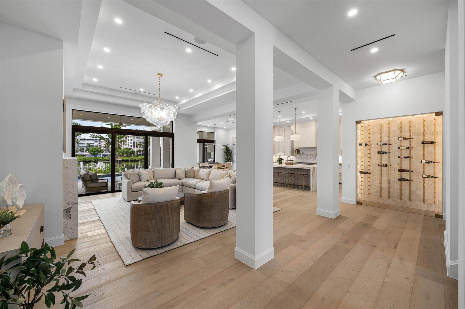 A bright, open-concept living room and kitchen area features light wood floors and a wine wall — 908 N Atlantic Drive, Lantana FL 33462, LANTANA, FL