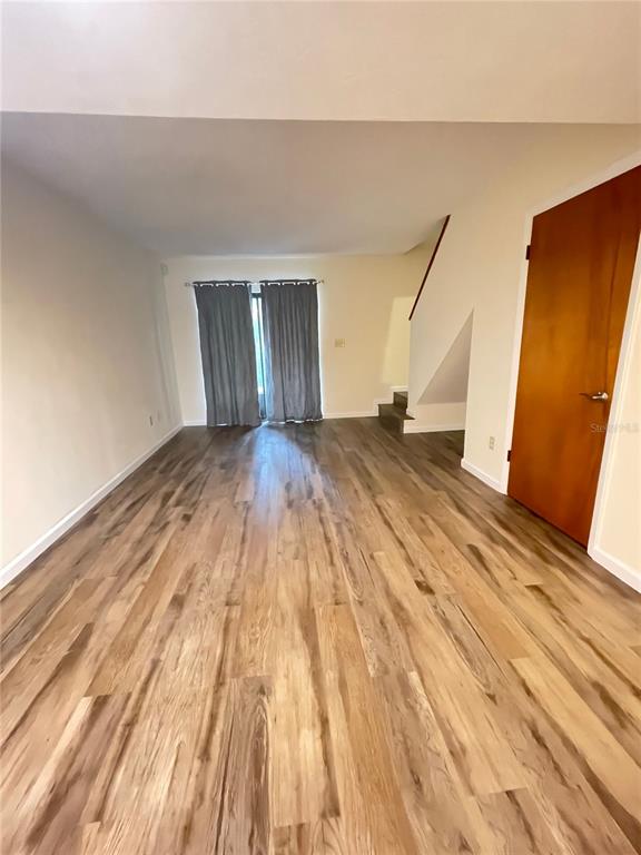 An empty room with wood-look flooring, gray curtains, and a wooden door — 914 SW 59TH TERRACE UNIT A, GAINESVILLE, FL