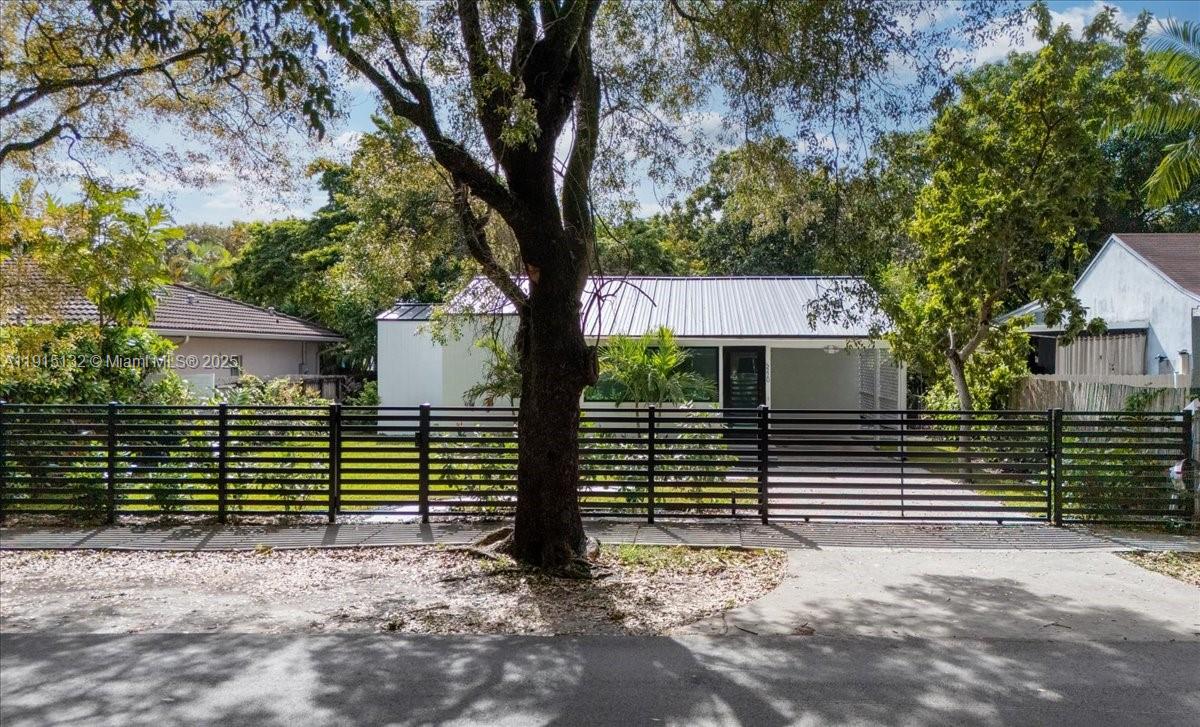 A single-story house with a metal roof is viewed behind a black horizontal slat fence — 5220 SW 6 ST, Miami FL 33134, MIAMI, FL
