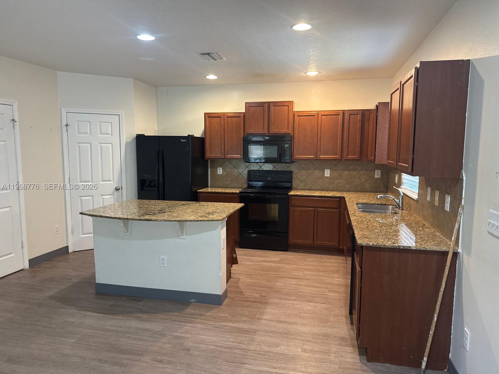 A kitchen features dark wood cabinets, granite countertops, black appliances, and a central island — 4717 Chatterton Way, Riverview FL 33578, RIVERVIEW, FL