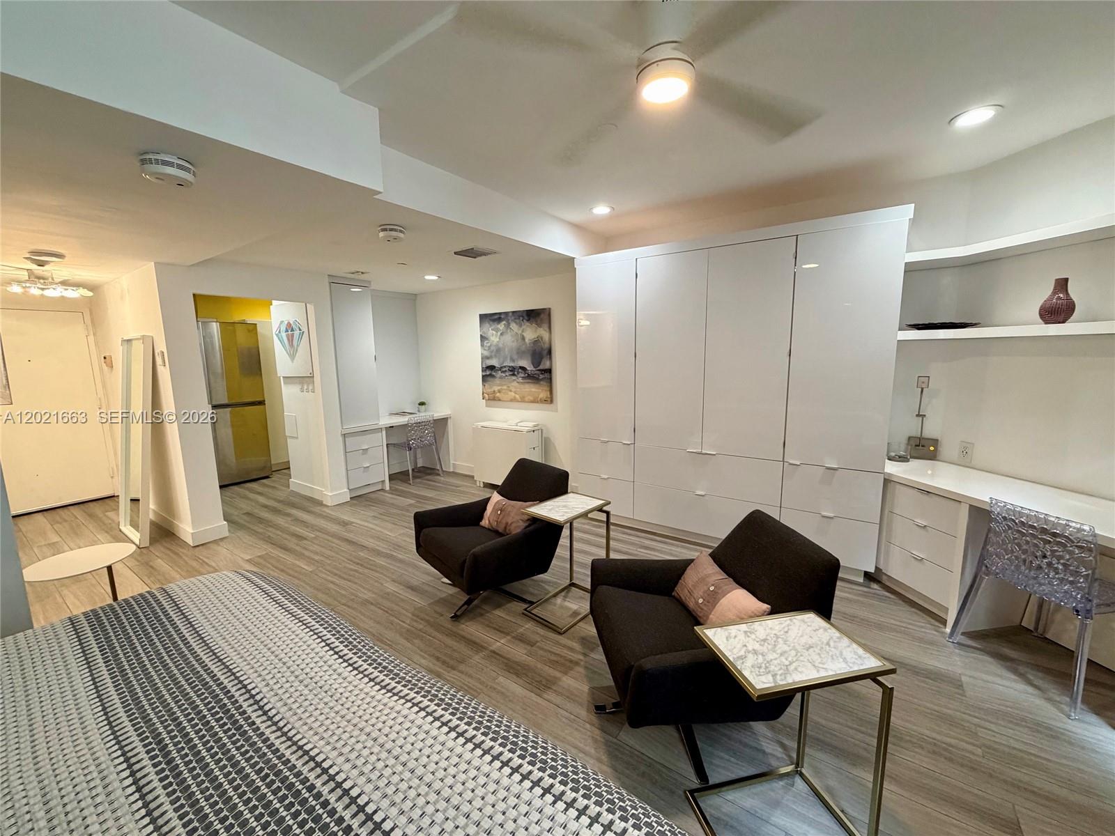 A modern bedroom features two dark armchairs, white cabinetry, a desk, and wood-look flooring — AVENTURA, FL