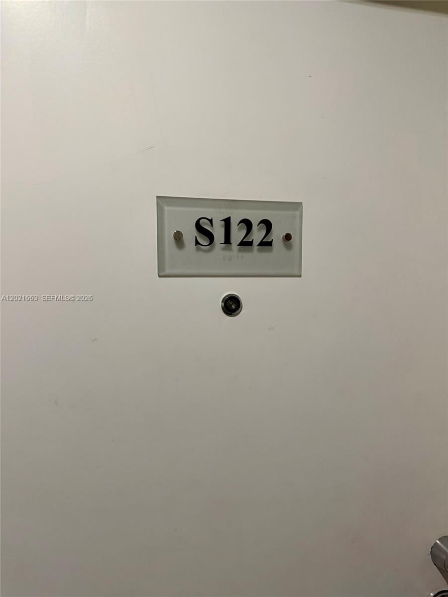 A white door features a rectangular sign labeled S122 and a circular peephole — AVENTURA, FL