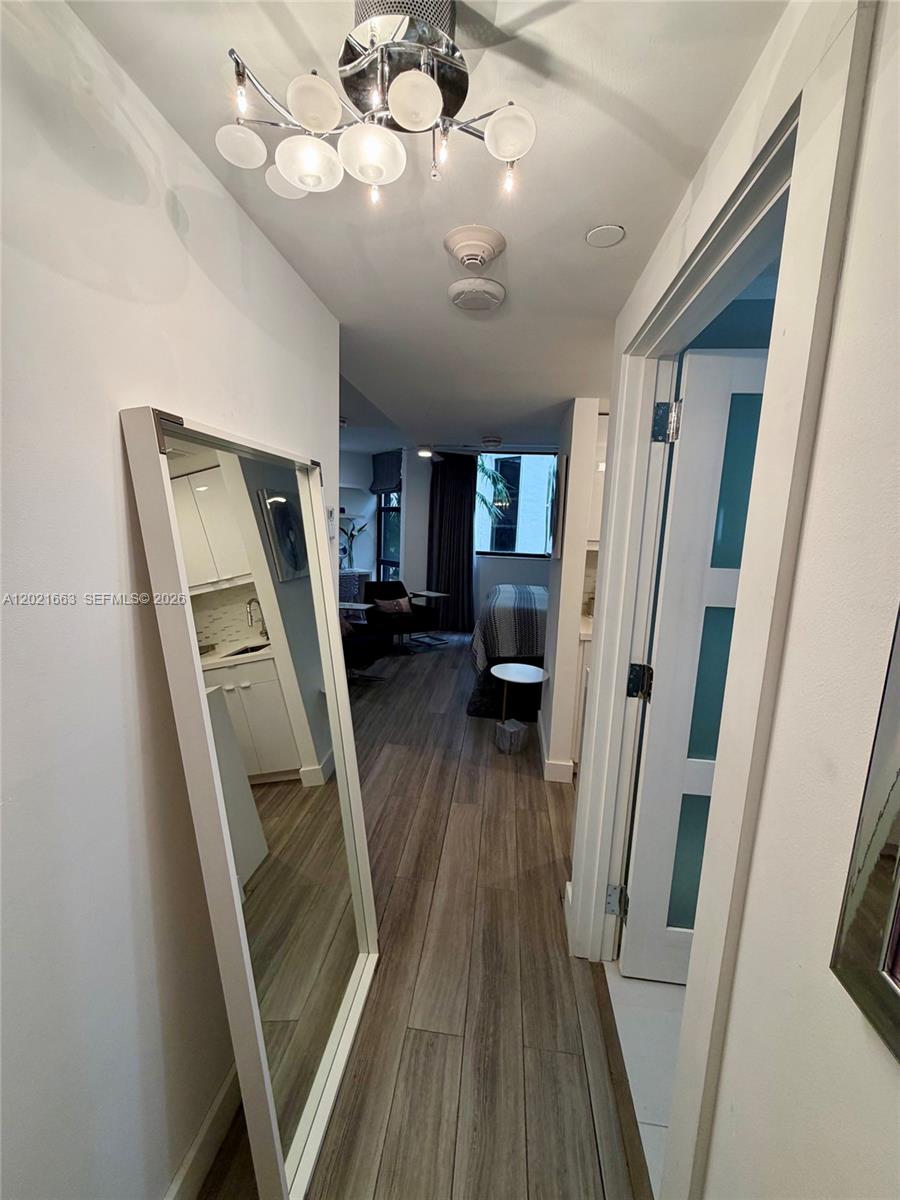 A hallway with wood-look flooring leads to a bedroom area featuring a large floor mirror — AVENTURA, FL