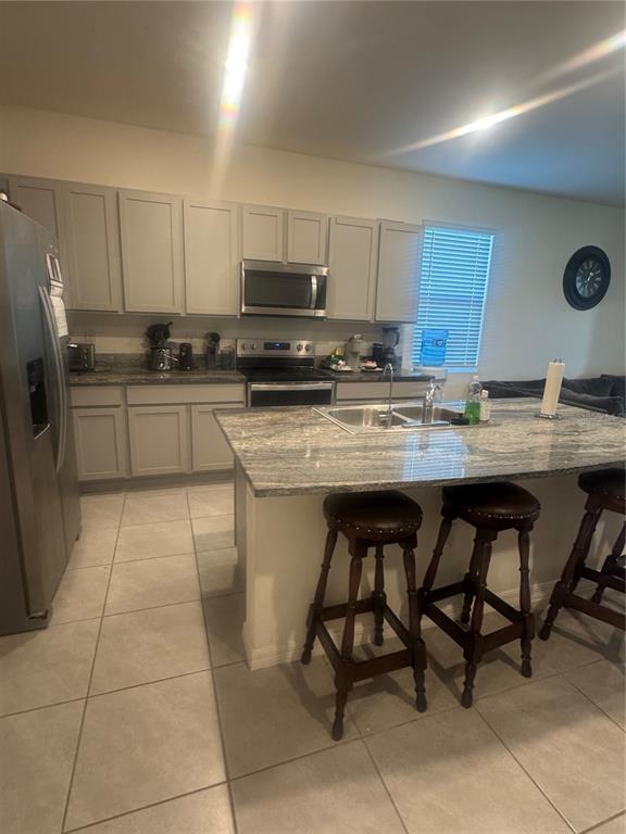 A kitchen features gray cabinets, granite countertops, a central island with bar stools, and tile flooring — 33074 TULIP PETAL LANE, WESLEY CHAPEL, FL
