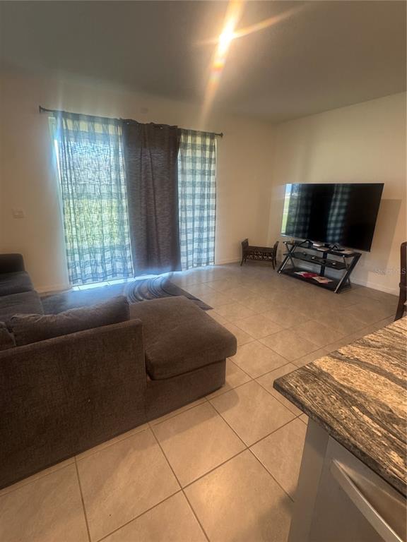 A living room with tile flooring, a gray sectional sofa, and a television on a stand — 33074 TULIP PETAL LANE, WESLEY CHAPEL, FL