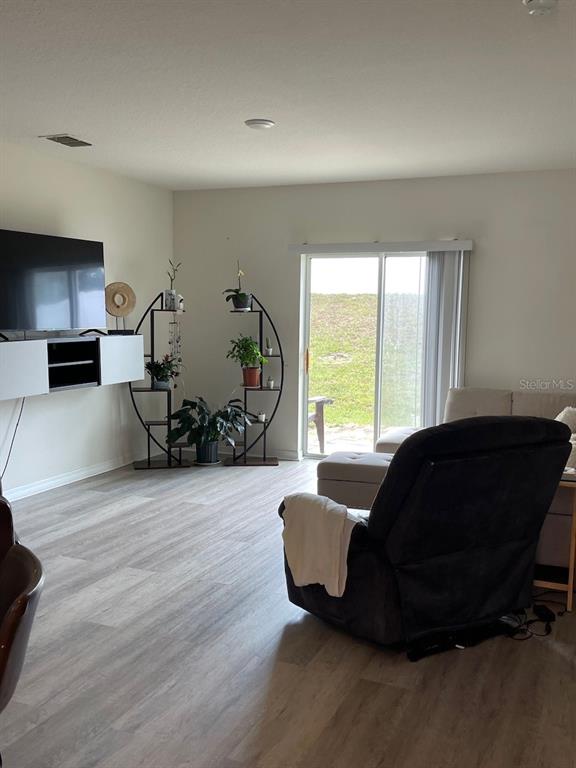 A living room features light wood-look flooring, a wall-mounted television, and a sliding glass door — 320 LIBERTY BOULEVARD, DAVENPORT, FL