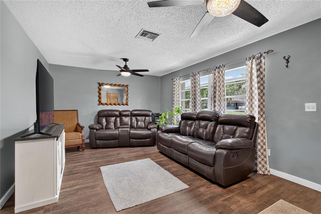 A living room features dark leather sofas, a television on a white console, and wood flooring — 555 WINOGENE AVE, UMATILLA, FL