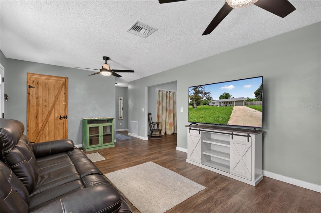 A living room features wood-look flooring, a leather sofa, a television console, and a barn door — 555 WINOGENE AVE, UMATILLA, FL