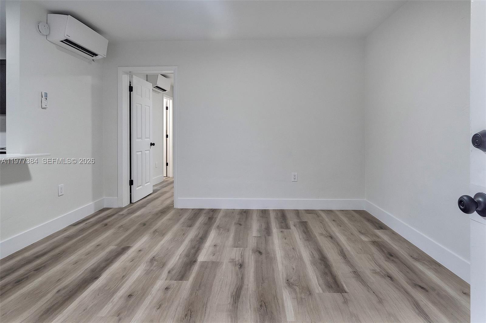 An empty room features white walls, wood-look flooring, and a wall-mounted air conditioning unit — 4037 SW 65th Ave # 11, South Miami FL 33155, SOUTH MIAMI, FL