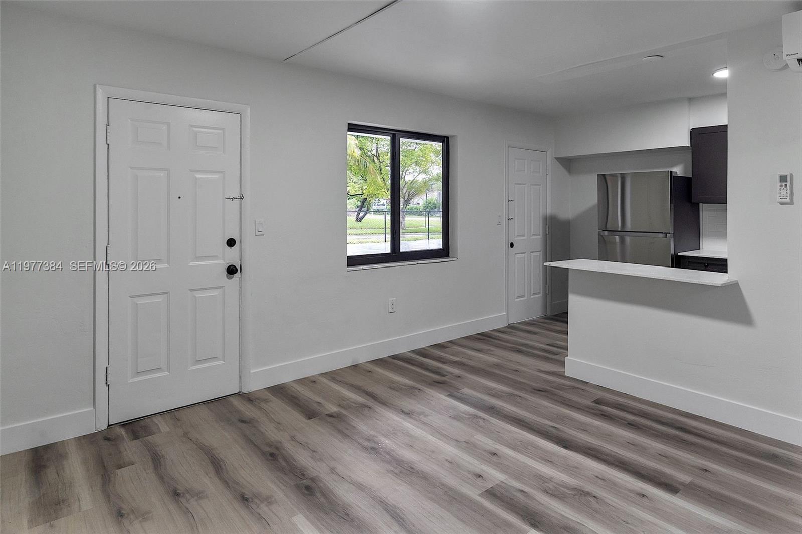 A room with light wood-look flooring, white walls, a window, and an open kitchen area — 4037 SW 65th Ave # 11, South Miami FL 33155, SOUTH MIAMI, FL
