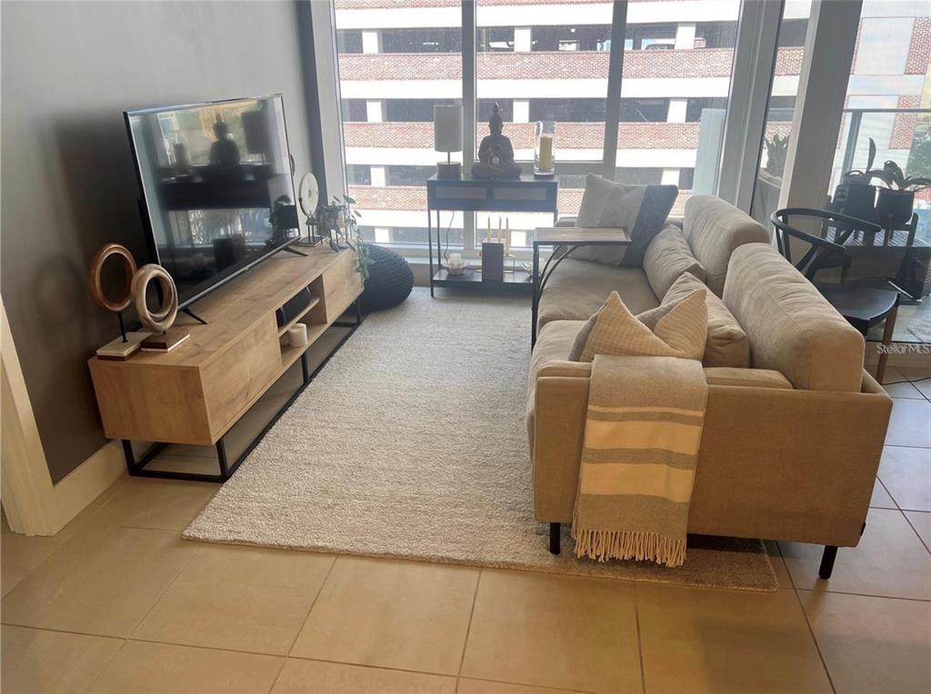 A living room features a beige sofa, a wood media console, and floor-to-ceiling windows — 145 2ND AVENUE S UNIT 614, ST PETERSBURG, FL