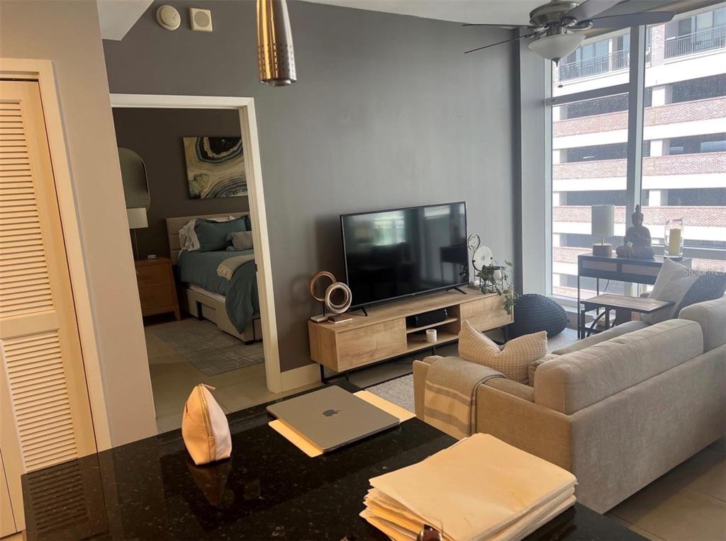 A living room with a television, wooden media console, and a view into a bedroom — 145 2ND AVENUE S UNIT 614, ST PETERSBURG, FL