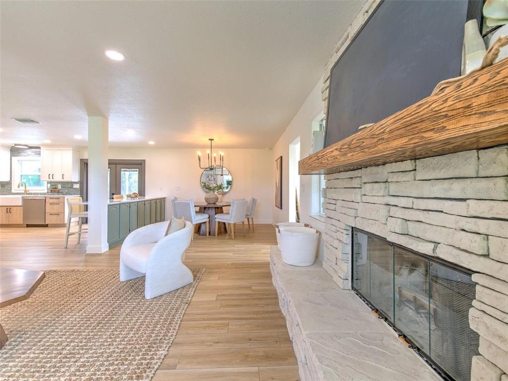 An open-concept living room features a stone fireplace, wood-look flooring, and an adjacent kitchen — 4608 HOLBROOK ROAD, PLANT CITY, FL