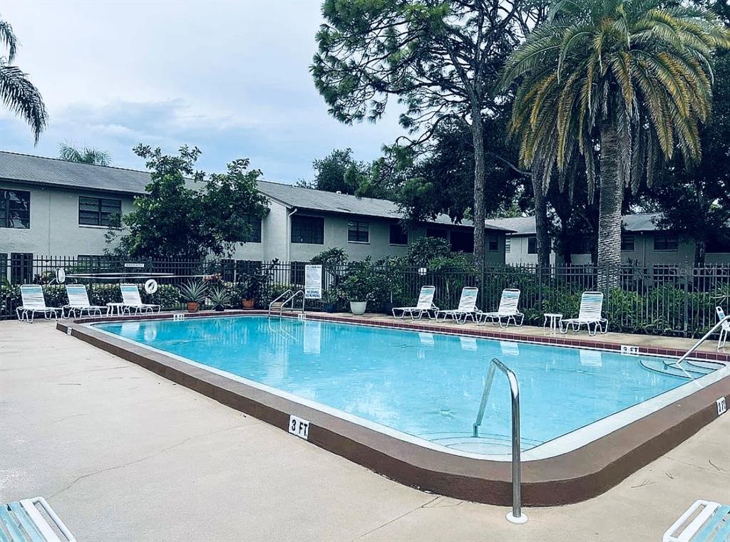 An outdoor swimming pool surrounded by lounge chairs and a metal fence near apartment buildings — 3032 EASTLAND BOULEVARD UNIT B202, CLEARWATER, FL