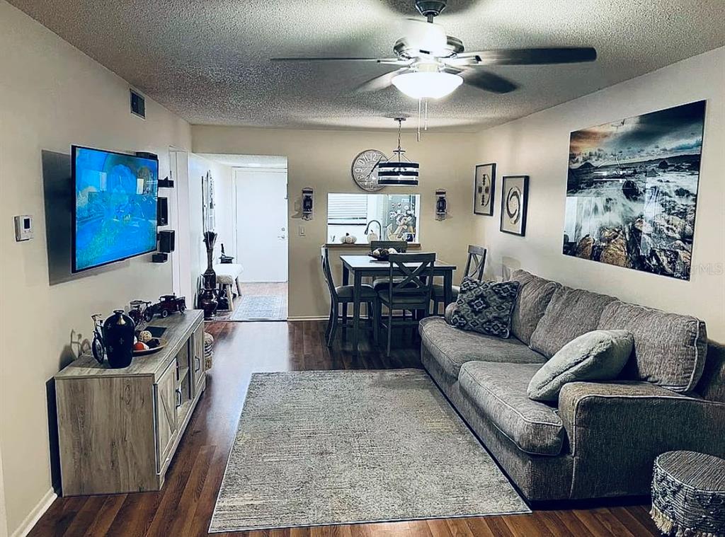 A living room with a gray sofa, wood-look flooring, a dining area, and a television — 3032 EASTLAND BOULEVARD UNIT B202, CLEARWATER, FL