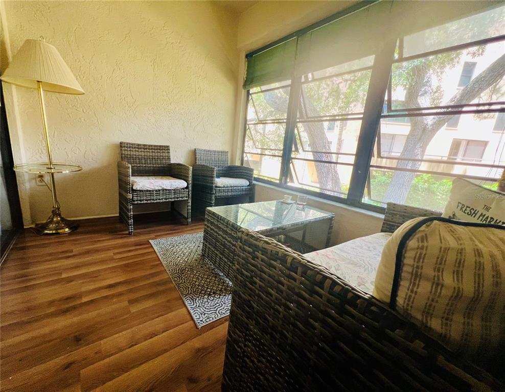 A sunroom features wicker furniture, a glass coffee table, wood-look flooring, and large windows — 3032 EASTLAND BOULEVARD UNIT B202, CLEARWATER, FL
