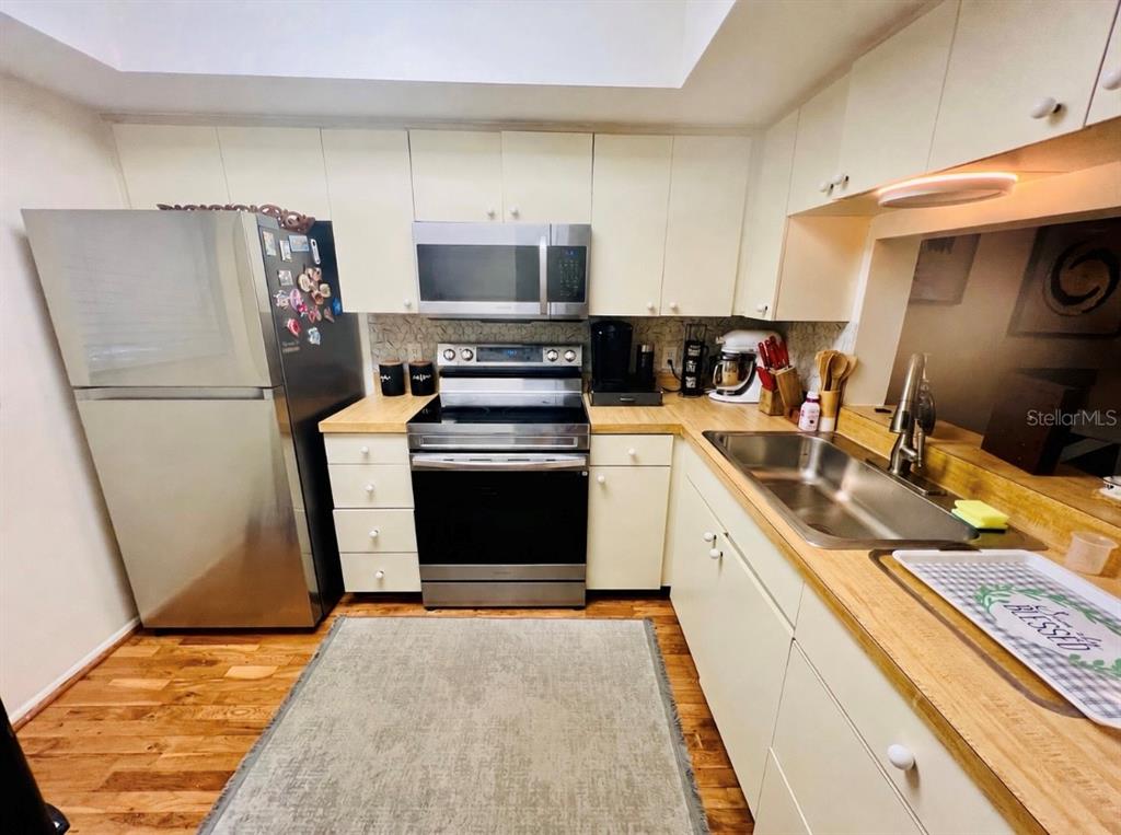 A kitchen features stainless steel appliances, light-colored cabinets, wood countertops, and hardwood flooring — 3032 EASTLAND BOULEVARD UNIT B202, CLEARWATER, FL