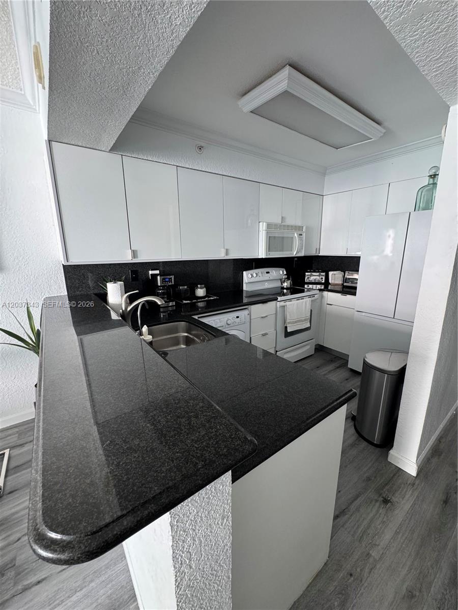 A kitchen features white cabinets, black countertops, stainless steel appliances, and gray wood-look flooring — 2501 S Ocean Dr # 1105, Hollywood FL 33019, HOLLYWOOD, FL