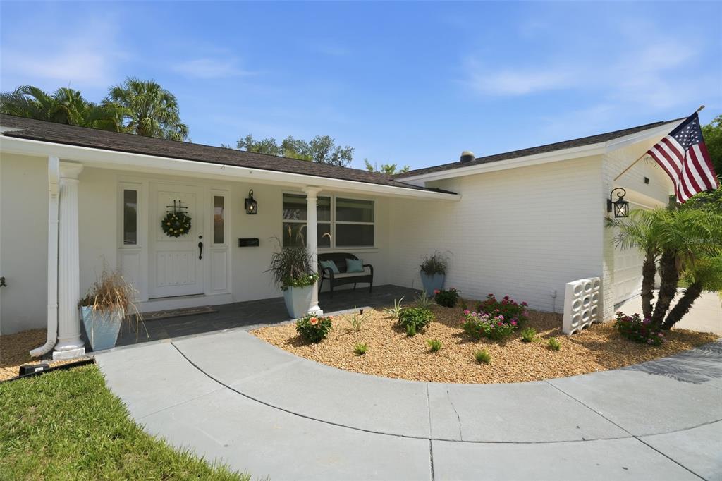 The exterior of a white brick house features a front porch, landscaping, and an American flag — 1819 MARYLAND AVENUE NE, ST PETERSBURG, FL