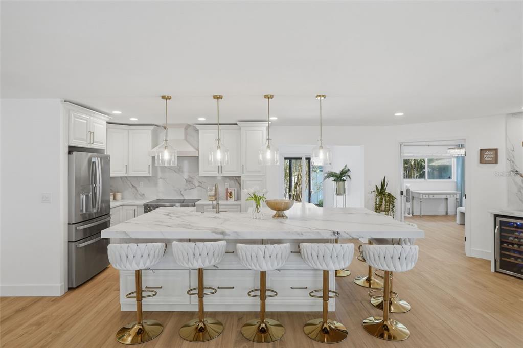 A modern white kitchen features a large marble-topped island with five gold-accented bar stools — 1819 MARYLAND AVENUE NE, ST PETERSBURG, FL