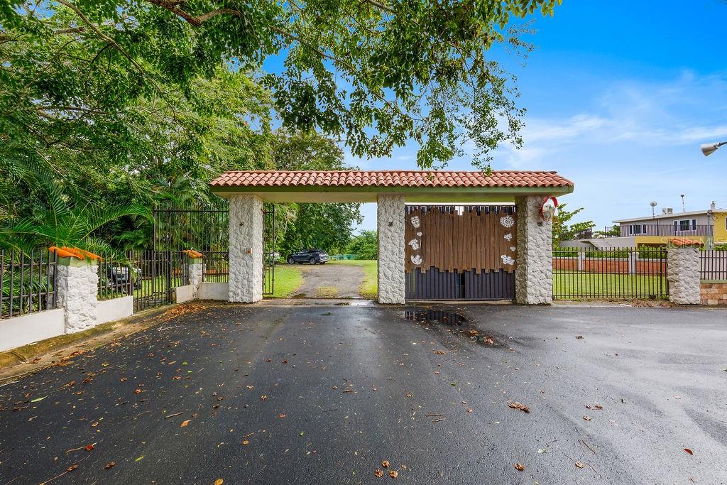 A gated entrance with a tiled roof, stone pillars, and a wooden gate — 690 LOS NABORIAS STREET, VEGA ALTA, PR
