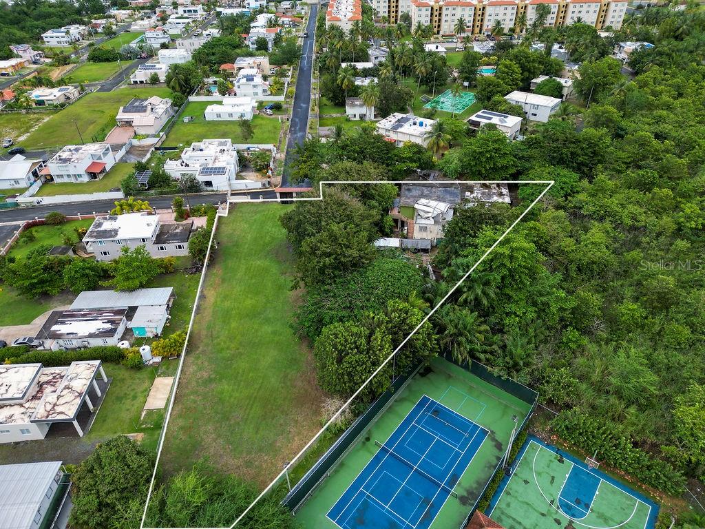 An aerial view shows a vacant grassy lot adjacent to a house and tennis court — 690 LOS NABORIAS STREET, VEGA ALTA, PR