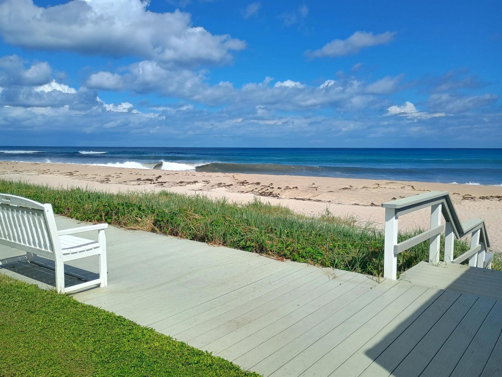 A white bench sits on a wooden deck overlooking a sandy beach and the ocean — 5505 N Ocean Boulevard # 106, Ocean Ridge FL 33435, OCEAN RIDGE, FL
