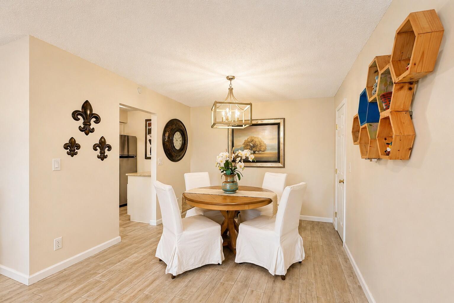 A dining room features a round wooden table, white slipcovered chairs, and hexagonal wall shelving — 9960 Pineapple Tree Drive # 109, Boynton Beach FL 33436, BOYNTON BEACH, FL