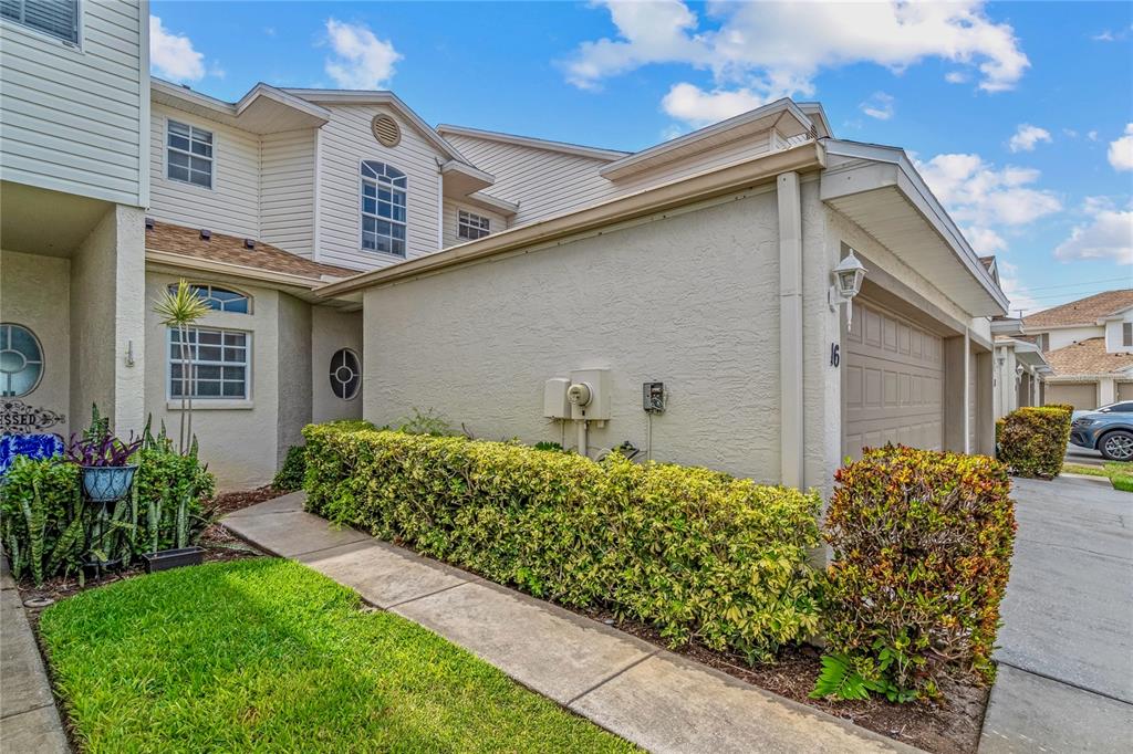 A two-story townhouse exterior features a beige stucco facade, a garage, and a landscaped hedge — 6400 46TH AVENUE N UNIT 16, KENNETH CITY, FL