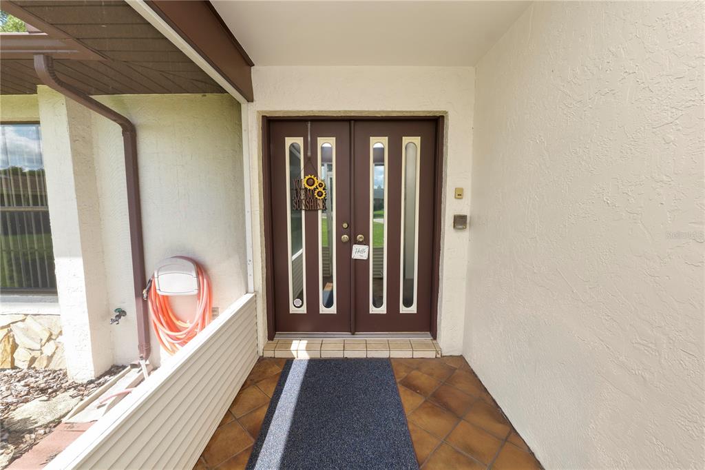 A covered entryway features a brown double door with vertical glass panels and tile flooring — 717 CEDAR KNOLL DRIVE S, LAKELAND, FL