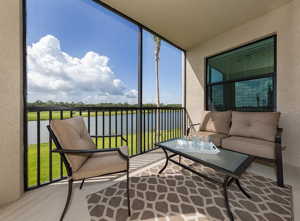 A screened-in balcony features patio furniture, a patterned rug, and a view of a lake — 16904 VARDON TERRACE UNIT 202, LAKEWOOD RANCH, FL
