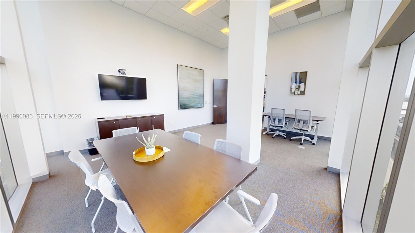 This office space features a conference table, chairs, a wall-mounted television, and neutral carpeting — 1501 Biscayne Blvd # 5C, Miami FL 33132, MIAMI, FL