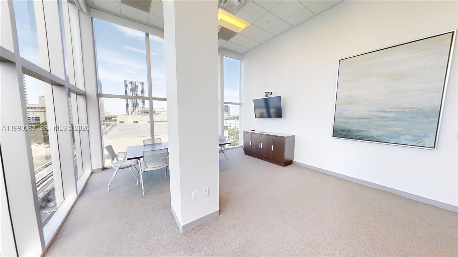 A bright office space features floor-to-ceiling windows, a conference table, and a wall-mounted television — 1501 Biscayne Blvd # 5C, Miami FL 33132, MIAMI, FL
