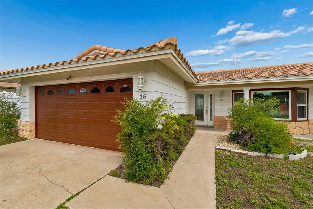 A single-story house exterior features a brown garage door, a tiled roof, and a walkway — 15 BELLEVUE DRIVE, TREASURE ISLAND, FL