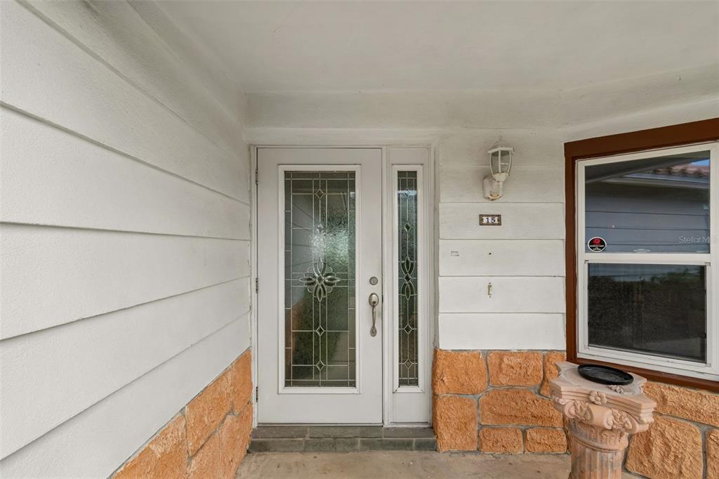 A white front door with decorative glass panels sits beside a window and stone siding — 15 BELLEVUE DRIVE, TREASURE ISLAND, FL