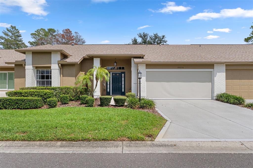 A single-story house features a tan exterior, white brick accents, a garage, and a front lawn — 18630 BENT PINE DRIVE, HUDSON, FL