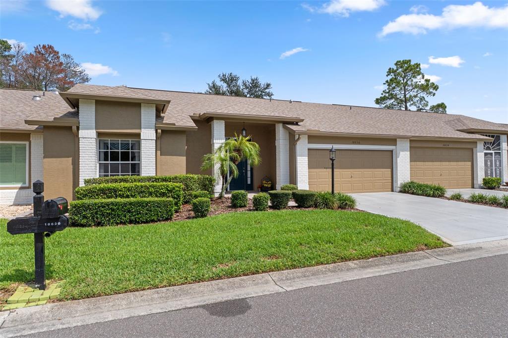 A single-story house features a tan stucco exterior, white brick accents, and two garage doors — 18630 BENT PINE DRIVE, HUDSON, FL