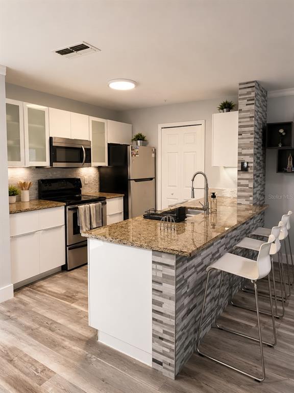 A kitchen features white cabinets, granite countertops, a tiled island, and stainless steel appliances — 5463 VINELAND ROAD UNIT 5203, ORLANDO, FL