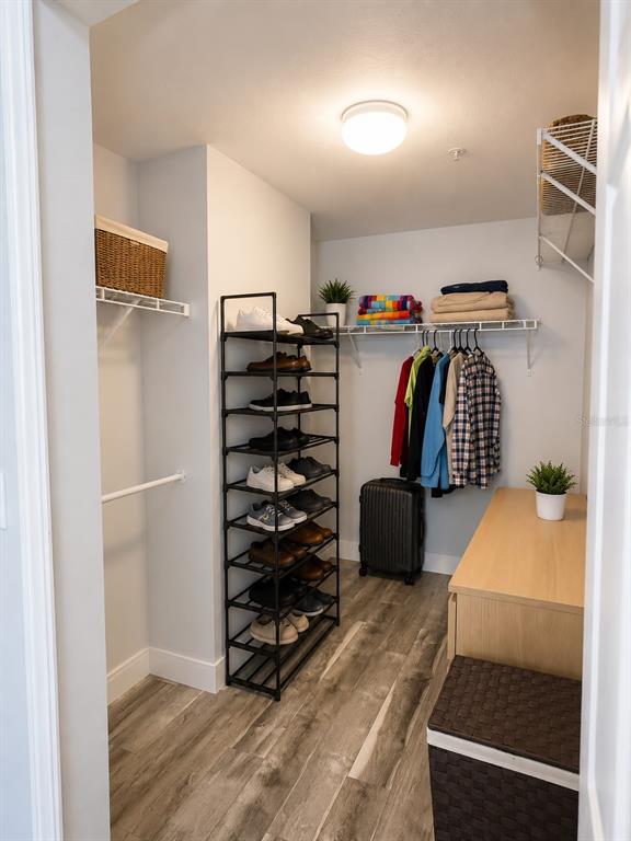 A walk-in closet features a tall shoe rack, hanging clothes, a dresser, and wood-look flooring — 5463 VINELAND ROAD UNIT 5203, ORLANDO, FL