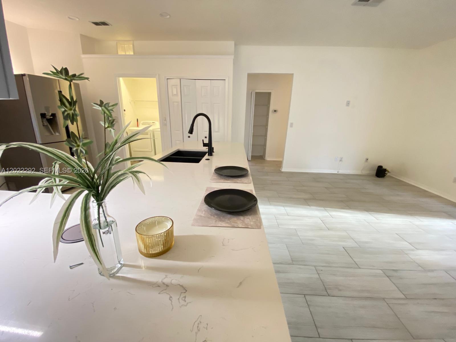 A kitchen island with a sink and two place settings overlooks an open living area — 3837 FALLSCREST, Clermont FL 34711, CLERMONT, FL