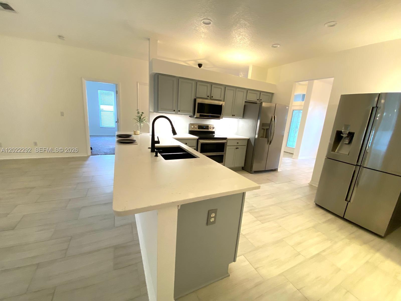 A kitchen features a white island, gray cabinets, stainless steel appliances, and light-colored tile flooring — 3837 FALLSCREST, Clermont FL 34711, CLERMONT, FL