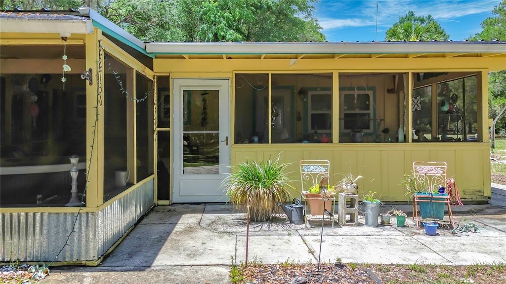 A yellow house features a screened-in porch with a concrete patio and potted plants — 22736 SW 117TH STREET, DUNNELLON, FL