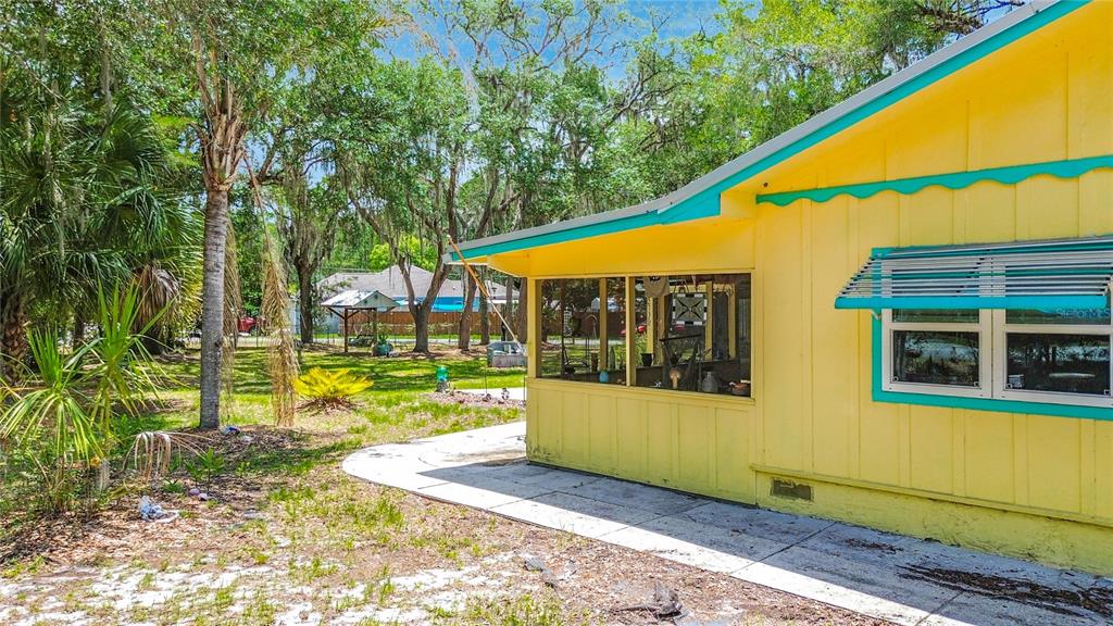 A yellow house with a screened-in porch and turquoise trim sits in a grassy yard — 22736 SW 117TH STREET, DUNNELLON, FL
