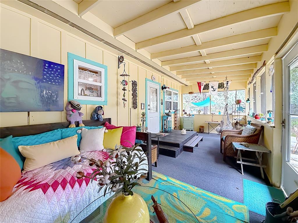 A sunroom features a daybed, wicker chair, yellow walls, and exposed ceiling beams — 22736 SW 117TH STREET, DUNNELLON, FL