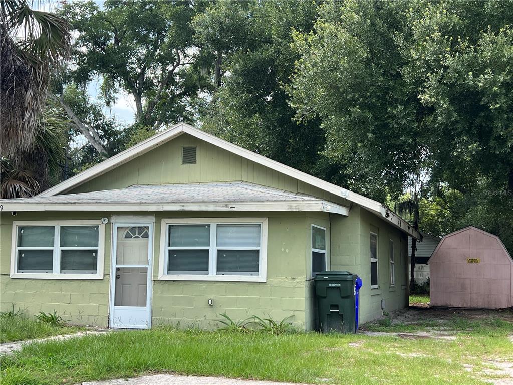 A single-story green house with a front door, multiple windows, and a detached storage shed — 519 W 12TH STREET, LAKELAND, FL