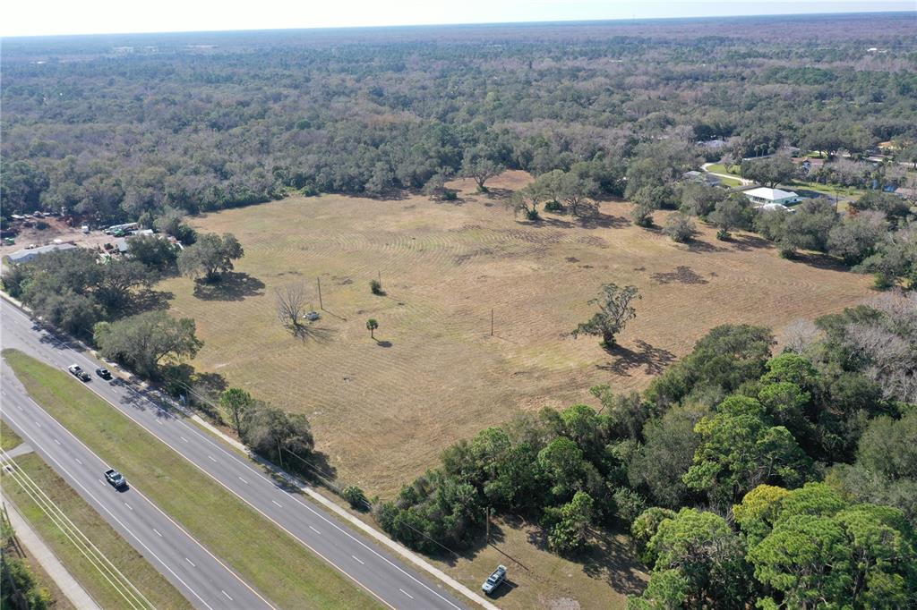 An aerial view shows a large, cleared grassy lot adjacent to a multi-lane highway — 4558 S RIDGEWOOD AVENUE, EDGEWATER, FL