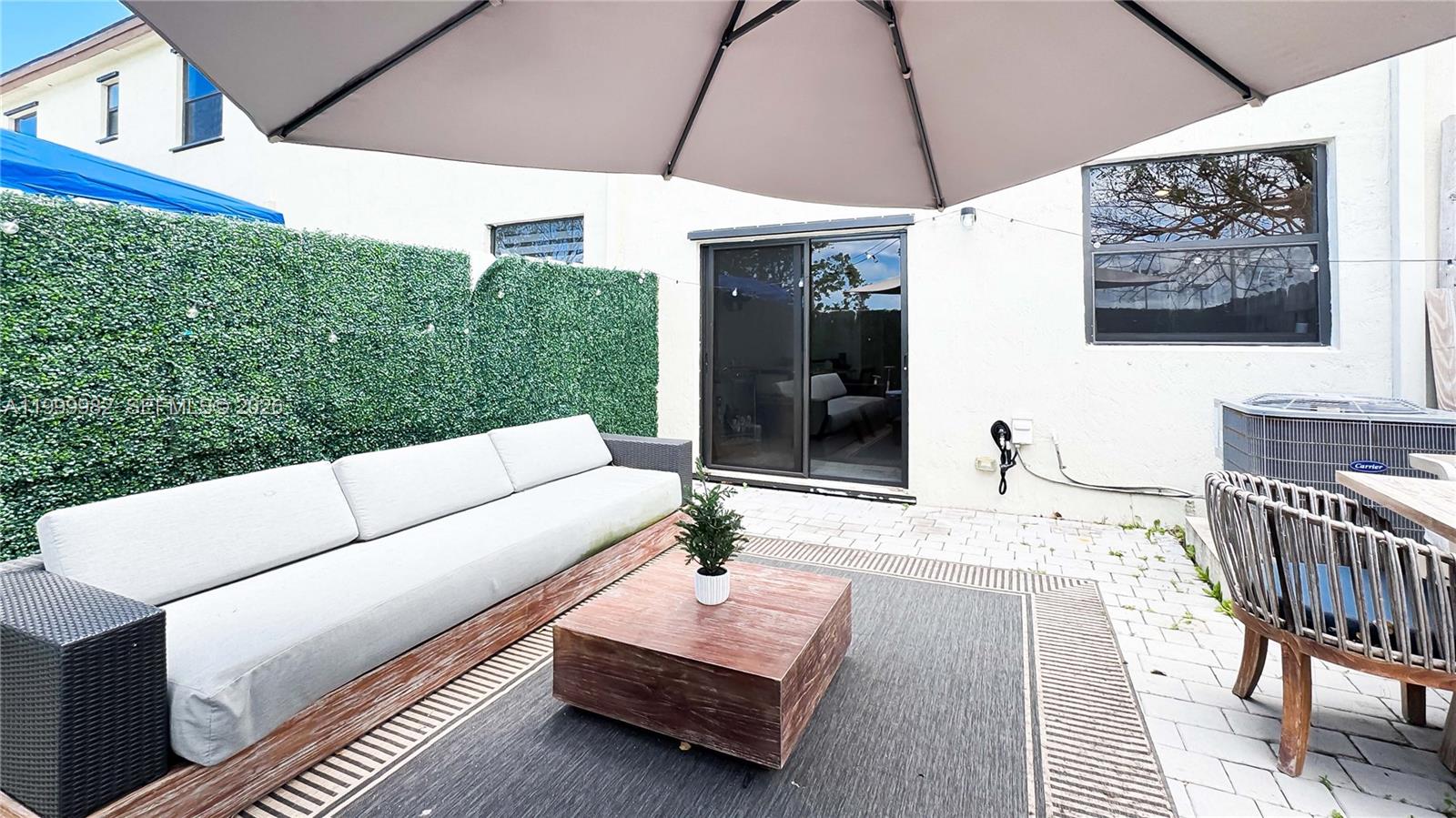 A patio features a sofa, a wooden coffee table, and an umbrella on a paved surface — 9949 SW 228th Ter, Miami FL 33190, MIAMI, FL